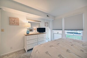 A bedroom with a bed, dresser, television, and a window with blinds. - Beautifully Renovated Condo in Sea Colony; Steps from Tennis, Tram and pool! (Bethany Beach)