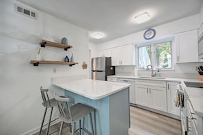 A modern kitchen with white cabinets, a stainless steel refrigerator, and a bar area with stools. - Beautifully Renovated Condo in Sea Colony; Steps from Tennis, Tram and pool! (Bethany Beach)