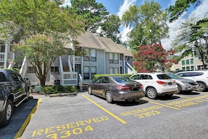 A parking lot with marked spaces, a building with a grey facade, and trees with pink flowers. - Beautifully Renovated Condo in Sea Colony; Steps from Tennis, Tram and pool! (Bethany Beach)
