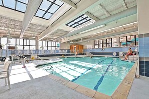 An indoor swimming pool with clear water, a diving board, and a lifeguard chair. - Beautifully Renovated Condo in Sea Colony; Steps from Tennis, Tram and pool! (Bethany Beach)