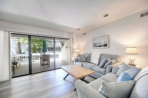 Ein modernes Wohnzimmer mit einem grauen Sofa, einem Holztisch und einer Glastür, die auf eine Terrasse im Freien führt.