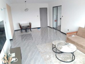 Ein modernes Wohnzimmer mit einer Couch, zwei Couchtischen, einem Essbereich mit Stühlen und einem Fernseher.