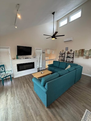 Ein Wohnzimmer mit Ecksofa, Flachbildfernseher, Kamin und Deckenventilator.