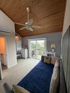 Ein Schlafzimmer mit einem Bett, einem Deckenventilator, einem Fenster und einer Tür, die auf einen Balkon führt.