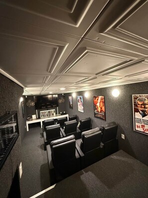 Ein Heimkino mit einem Flachbildfernseher, mehreren Sitzbereichen und einer Sammlung von Filmplakaten an den Wänden.
