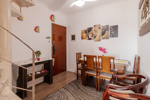 Ein Essbereich mit einem Holztisch und Stühlen, einer kleinen Topfpflanze und einem an der Wand befestigten Regal.