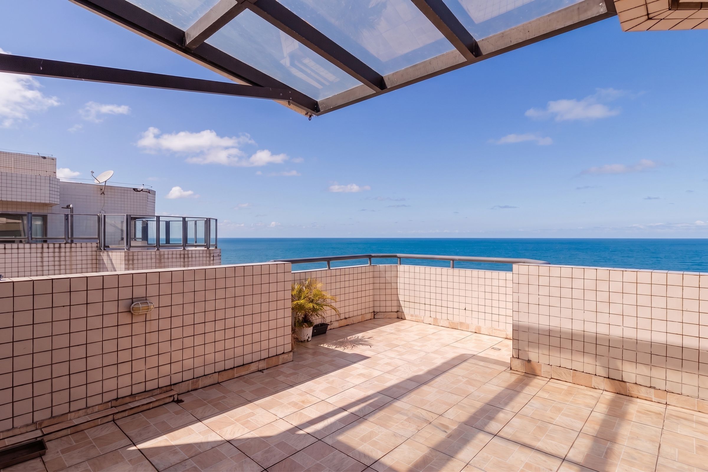 Una terrassa al terrat amb vista al mar, paviment de rajola i una planta en test.