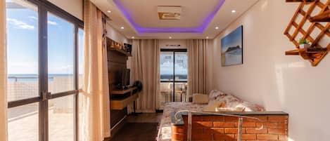 A modern bedroom with a large window, a bed, a desk, and a view of the sea.