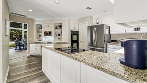 Una cocina moderna con armarios blancos, un refrigerador de acero inoxidable, un horno empotrado y una encimera de granito.