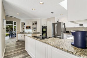 A modern kitchen with white cabinetry, a stainless steel refrigerator, a built-in oven, and a granite countertop. - Sunset Rentals | Starboard Tack 40 (Hilton Head Island)