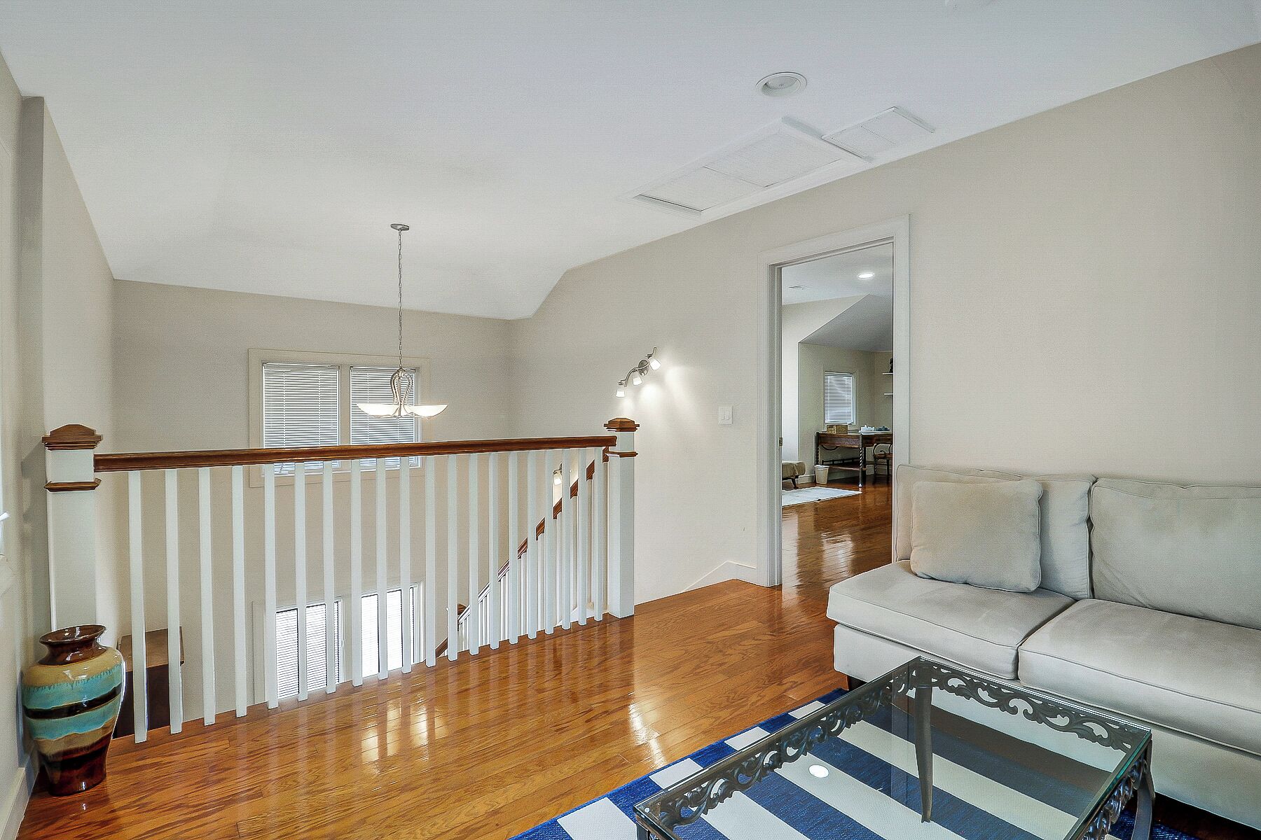 A spacious living room with a wooden staircase, a glass coffee table, and a sofa.