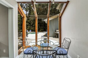 A glass-enclosed patio with a table and chairs, a grill, and a pool in the background. - Sunset Rentals | Starboard Tack 40 (Hilton Head Island)