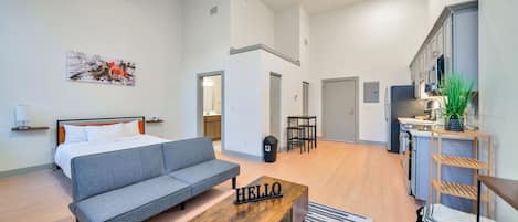 A modern hotel room with a bed, sofa, coffee table, and kitchenette.