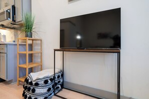 Une cuisine moderne avec un téléviseur à écran plat encastré sur un meuble en bois, un tabouret en bois avec un coussin à motifs et une plante en pot.