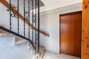 Eine Treppe mit hölzernem Geländer und schwarzen Metallspindeln, die zu einer Holztür führt.