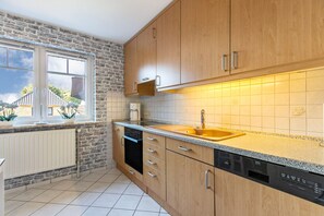 Eine Küche mit Holzausstattung, einem Backofen, einem Geschirrspüler und einem Fenster mit Blick ins Freie.