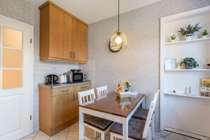 A compact kitchen with wooden cabinets, a microwave, a kettle, and a dining table with chairs. - Apartment 'Perle Im Eidertal' with Balcony and Wi-Fi (Pahlen)