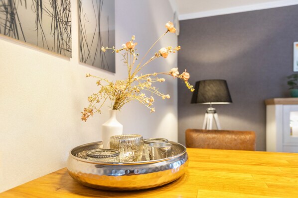 Ein Esstisch mit einer dekorativen Schale, darin eine Vase mit getrockneten Blumen und einem Kerzenständer.