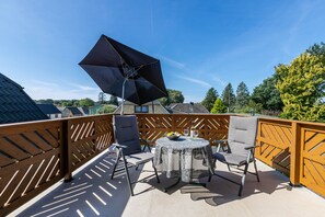 Eine Terrasse mit einem runden Tisch, zwei Stühlen, einem großen Sonnenschirm und einem Holzzaun.