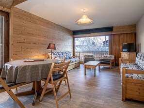 A cozy cabin interior with a wooden interior, a dining table with chairs, a sofa, and a television. - Apartment in Morzine center - 4 guests (Morzine)
