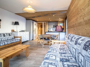 Ein gemütlicher Innenraum mit Holzbalkendecke, einer Couch, einer Bank, einem Esstisch mit Stühlen und einer Küchenzeile.