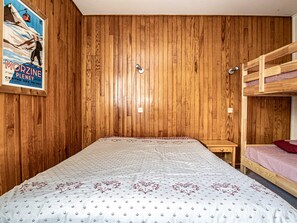 A room with wooden panel walls, a bunk bed, a single bed with patterned bedding, a small table, and a poster on the wall. - Apartment in Morzine center - 4 guests (Morzine)