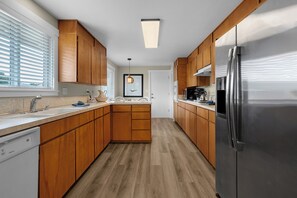 A modern kitchen with wooden cabinets, a stainless steel refrigerator, and a window with blinds. - THAT'S WHAT SEA SAID at Seaside Beach (Seaside)