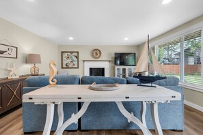 A modern living room with a sofa set, a white coffee table, a fireplace, a television, and a sailboat model. - THAT'S WHAT SEA SAID at Seaside Beach (Seaside)