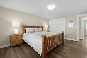 A bedroom with a wooden bed, two bedside tables with lamps, a white door, and a hallway. - THAT'S WHAT SEA SAID at Seaside Beach (Seaside)