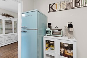 A kitchen with a light blue refrigerator, a coffee maker, a toaster, and a cabinet with kitchen utensils. - Escape to this bright, pet-friendly cottage just minutes from Perdido Key's sugar-white sands! Two queen bedrooms sleep 4, plus a full kitchen, in-unit laundry, screened front porch & fenced backyard. Free driveway parking for 4! (Pensacola)