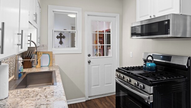 A kitchen with white cabinets, a stainless steel microwave, a black stove, and a window with a decorative item. - Escape to this bright, pet-friendly cottage just minutes from Perdido Key's sugar-white sands! Two queen bedrooms sleep 4, plus a full kitchen, in-unit laundry, screened front porch & fenced backyard. Free driveway parking for 4! (Pensacola)