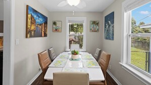 A dining area with a table set for four, surrounded by chairs, with artwork on the walls and a ceiling fan above. - Escape to this bright, pet-friendly cottage just minutes from Perdido Key's sugar-white sands! Two queen bedrooms sleep 4, plus a full kitchen, in-unit laundry, screened front porch & fenced backyard. Free driveway parking for 4! (Pensacola)