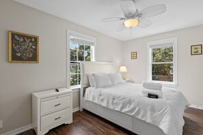 A bedroom with a bed, nightstand, dresser, and a ceiling fan. - Escape to this bright, pet-friendly cottage just minutes from Perdido Key's sugar-white sands! Two queen bedrooms sleep 4, plus a full kitchen, in-unit laundry, screened front porch & fenced backyard. Free driveway parking for 4! (Pensacola)