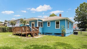 A residential house with a blue exterior, a wooden deck, and a grassy yard. - Escape to this bright, pet-friendly cottage just minutes from Perdido Key's sugar-white sands! Two queen bedrooms sleep 4, plus a full kitchen, in-unit laundry, screened front porch & fenced backyard. Free driveway parking for 4! (Pensacola)