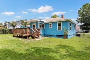 A residential house with a blue exterior, a wooden deck, and a grassy yard. - Escape to this bright, pet-friendly cottage just minutes from Perdido Key's sugar-white sands! Two queen bedrooms sleep 4, plus a full kitchen, in-unit laundry, screened front porch & fenced backyard. Free driveway parking for 4! (Pensacola)
