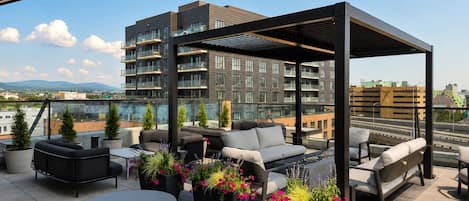 A rooftop terrace with outdoor seating, potted plants, and a view of a cityscape.