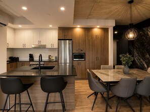 A modern kitchen with a central island, stainless steel appliances, and a dining area with a marble table and chairs. - Rooftop Pool | Private Terrace | Signature 908 (Québec)