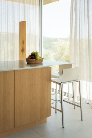 A kitchen area with a wooden cabinet, a white countertop, a wicker fruit basket, and a white chair. - Villa Epicurean Retreat - Luxurious villa, infinity pool, sea view in Finikounda (Finikounda)
