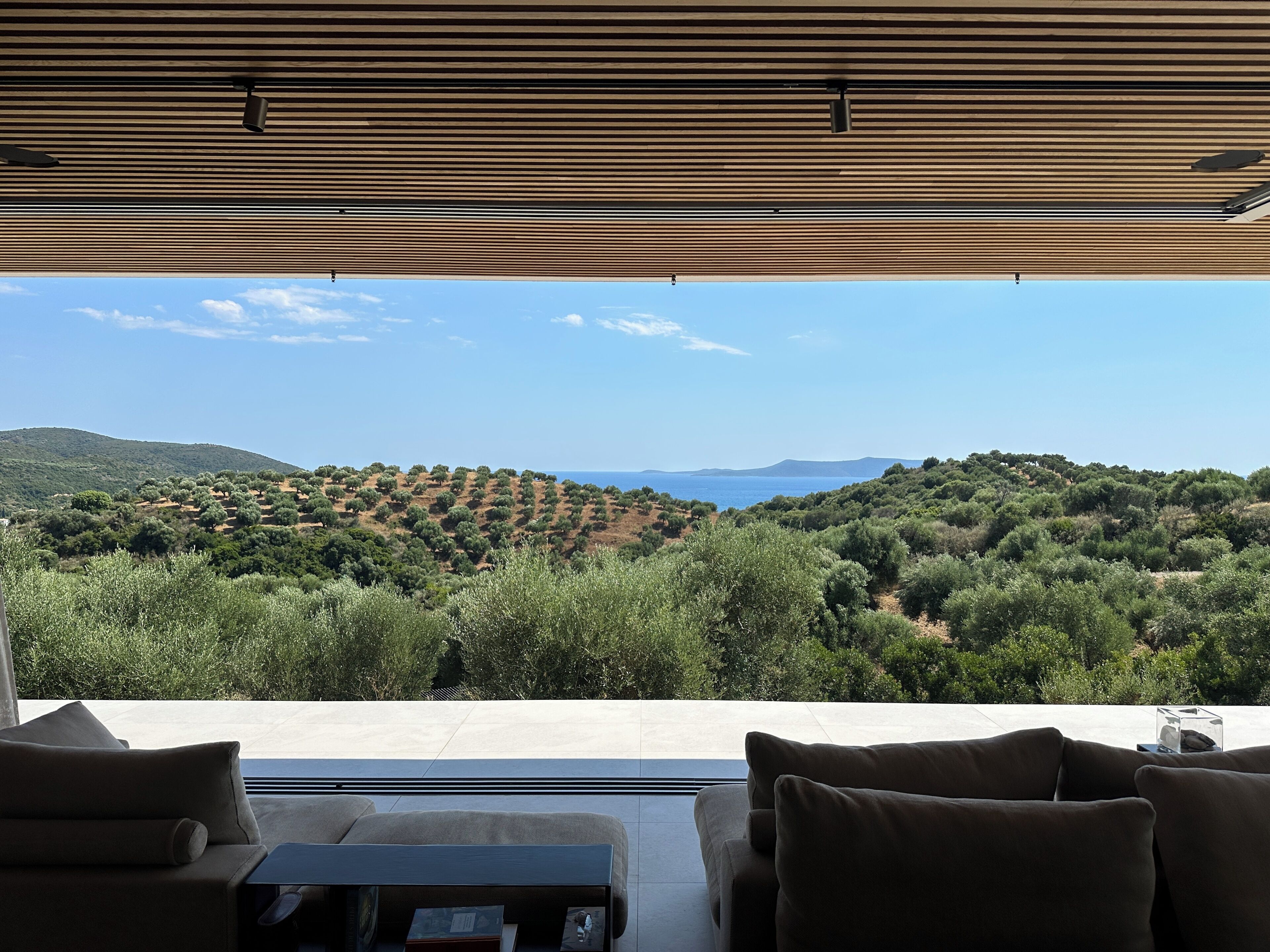 A modern outdoor seating area with a view of a hilly landscape and the sea.