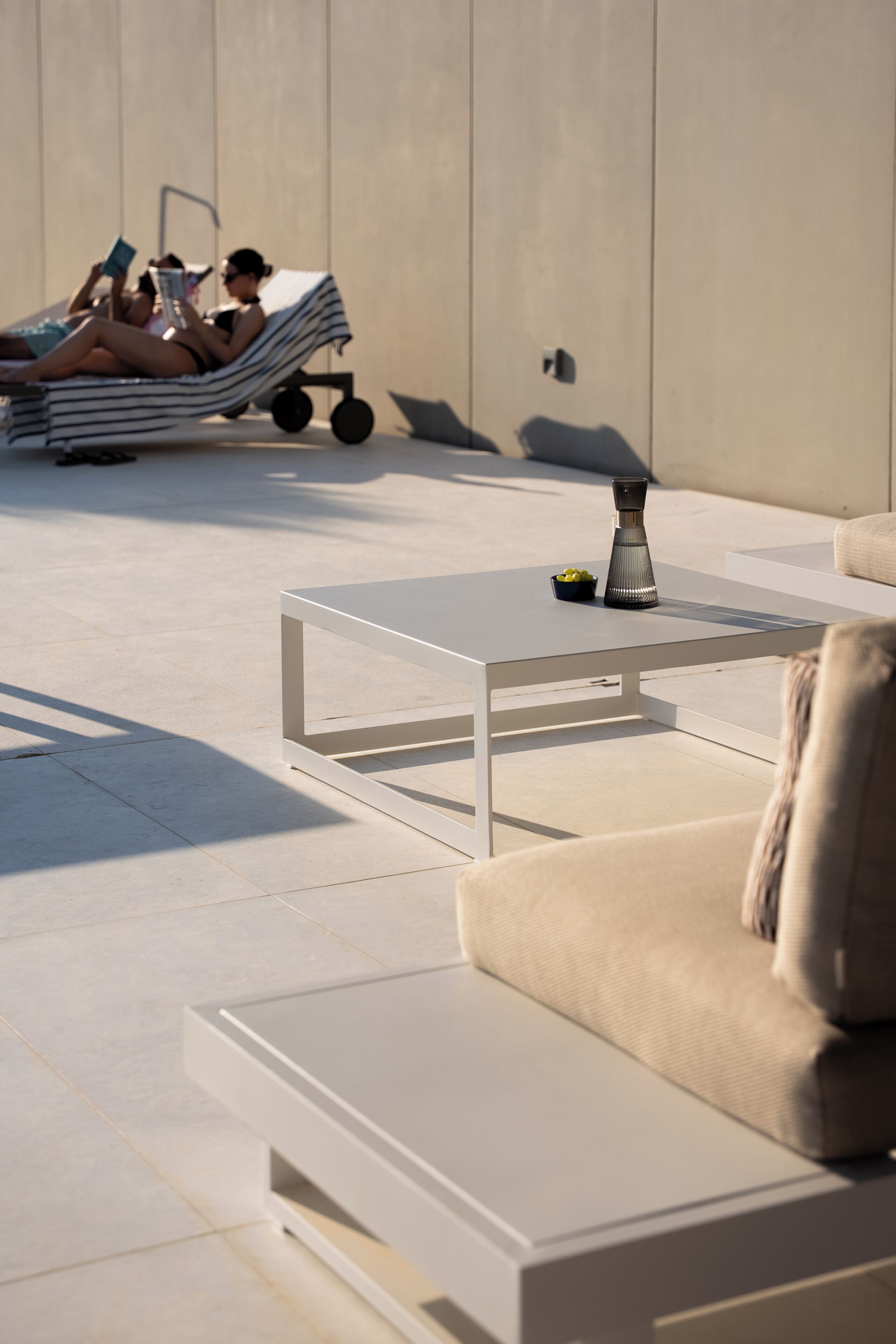 A modern outdoor seating area with a white table and a sofa, a small bowl of fruit, and a decorative vase.