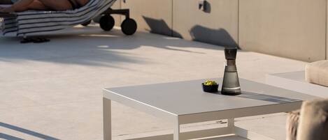 A modern outdoor seating area with a white table and a sofa, a small bowl of fruit, and a decorative vase.