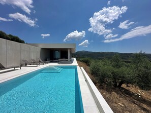 Une piscine extérieure moderne, dotée de chaises longues et d’un bâtiment avec une porte en verre.