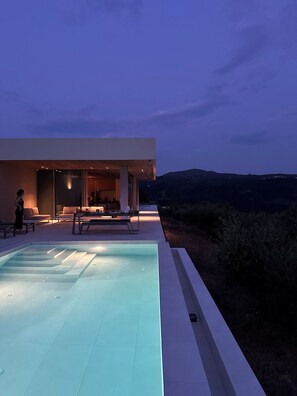 Une maison moderne dotée d’une piscine, d’un espace salon extérieur et offrant une vue sur les collines.