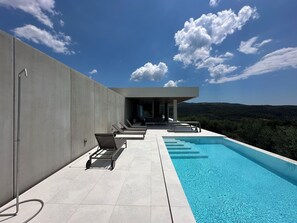 Un área de piscina moderna al aire libre con sillones de descanso y vistas al paisaje.