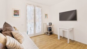 Un salon moderne avec un canapé, une machine à café posée sur une étagère, une table blanche et un grand téléviseur fixé au mur.