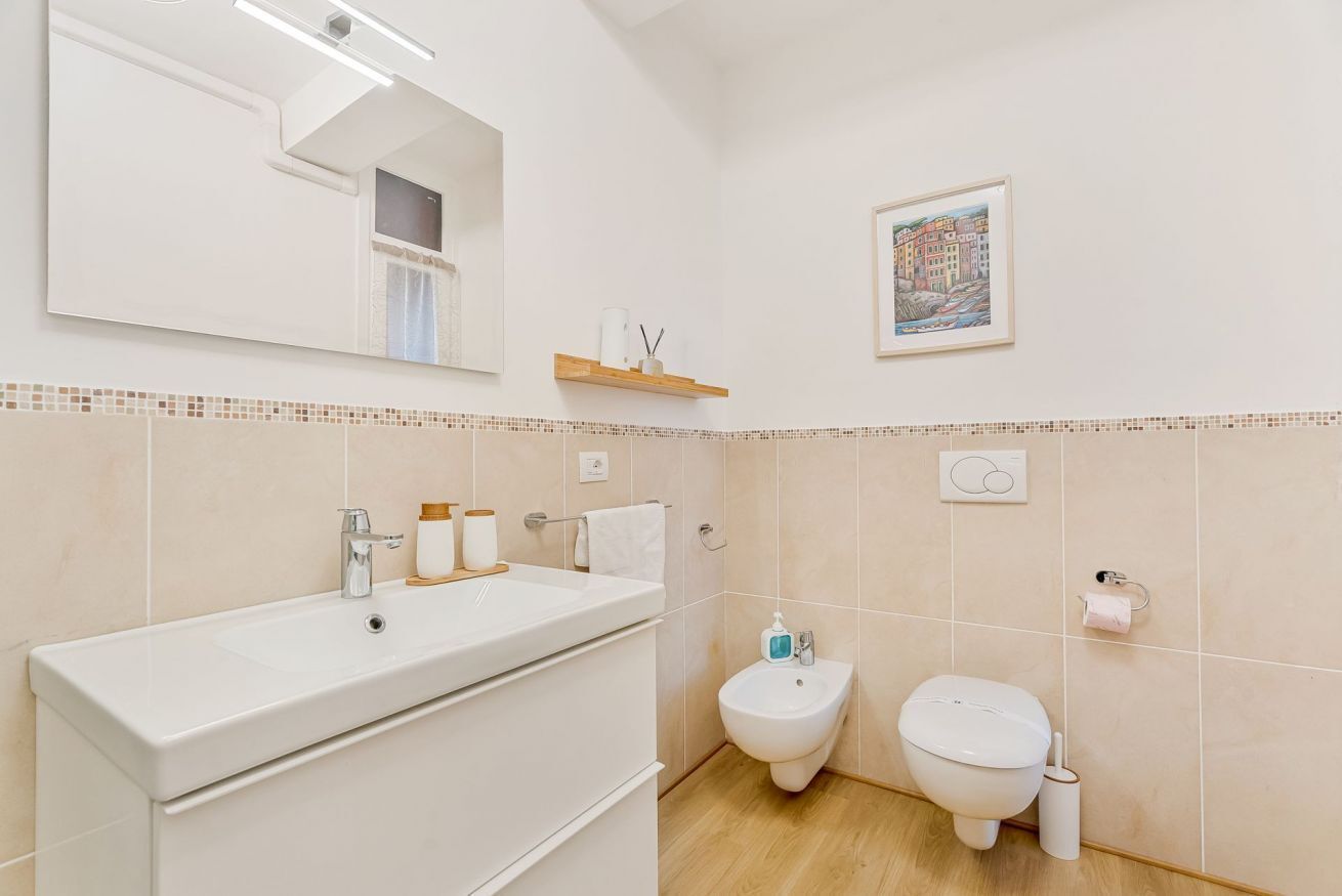 A bathroom with a white sink, bidet, and toilet, a mirror, and a framed picture on the wall.