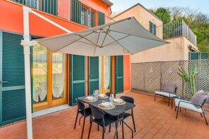 Eine Terrasse im Freien mit Esstisch und Stühlen, beschattet durch einen Sonnenschirm.