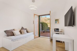 Ein modernes Zimmer mit einem weißen Sofa, einem kleinen Tisch, einem Fernseher und einer Schiebetür zu einem Außenbereich.