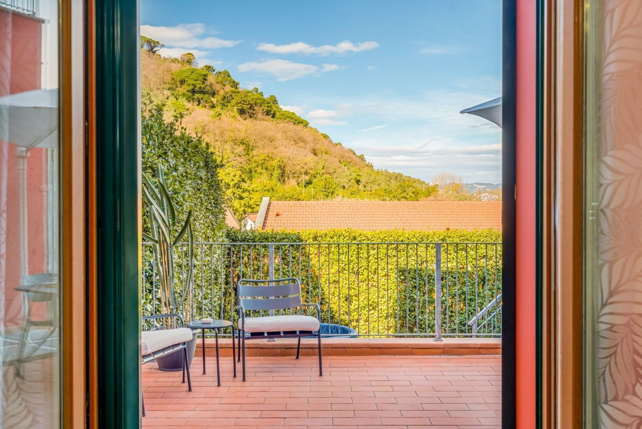 A balcony with a view of a hillside, a chair, and a table.