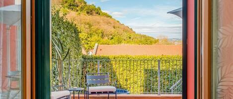 A balcony with a view of a hillside, a chair, and a table.